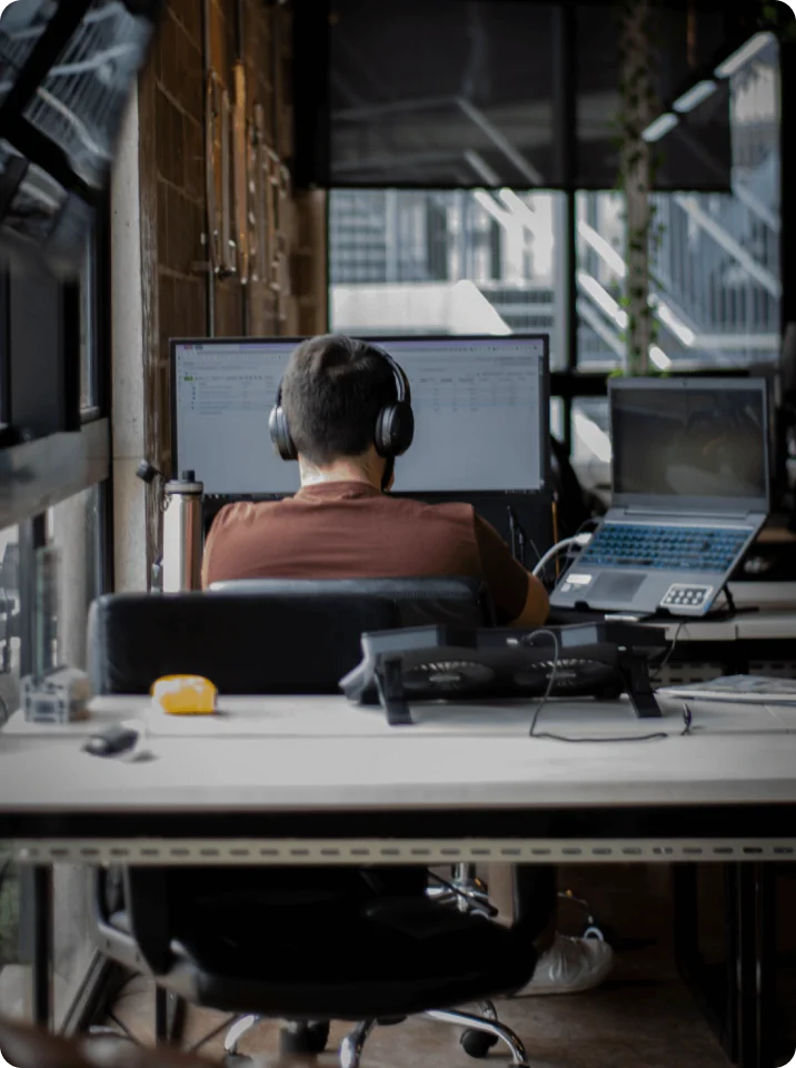 Integrante da Cluster trabalhando com fones de ouvido em uma estação com monitor e notebook, no escritório da empresa