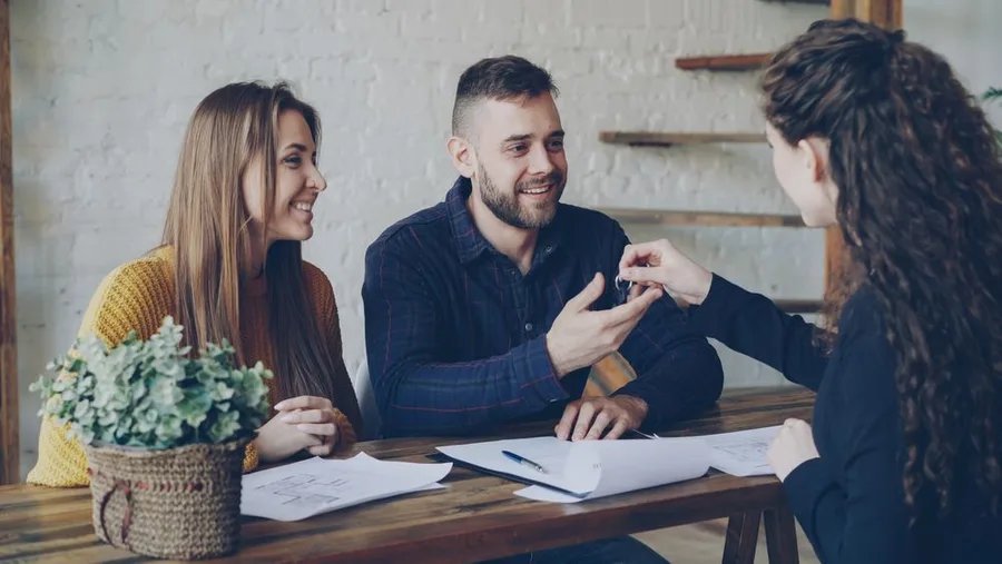 Corretora entregando as chaves de um imóvel a um casal durante o atendimento